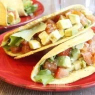 Dos tacos de ensalada de aguacate sobre plato rojo de cerámica para comer sin carne.