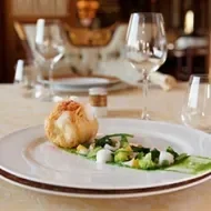 Elegante platillo de merluza en salsa verde servido en una mesa junto a copas.