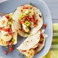 Plato con tres tacos de mariscos listos para ser degustados.