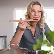 Mujer sonriente cocinando en la cocina probando salsa de tomate.