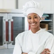 Una chef de pie con los brazos cruzados y vistiendo un uniforme.