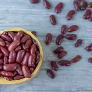 Primer plano de frijoles en cuchara de madera sobre fondo de color gris.
