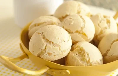 Una fotografía en tonos amarillos muestra una encimera de madera verdosa, un pequeño paño blanco con lunares amarillos y un recipiente amarillo con varios panes de queso en su interior. Al fondo, una taza de café blanca.
